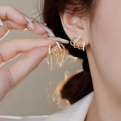 Woman wearing a gold claw earring with sparkling stones while holding the other pair-mate up in manicured fingers 2