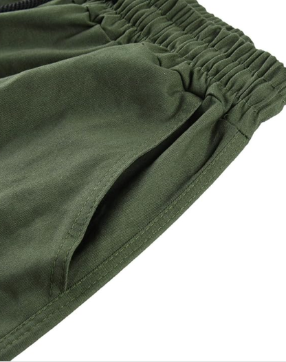 Close-up of the olive green elasticated waistband and the stitched side pocket opening on the trousers. 13