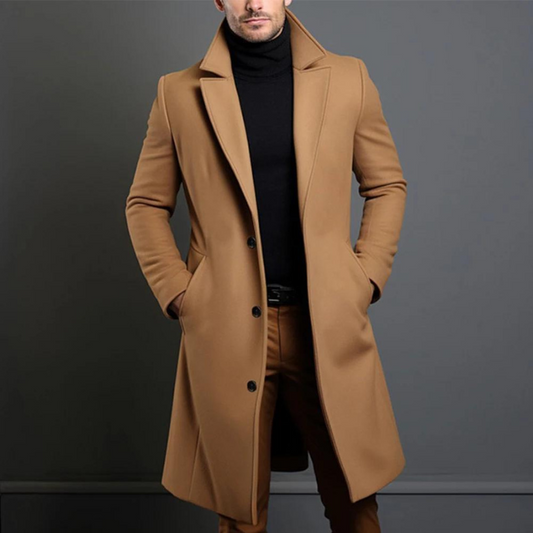 Model wearing the camel version of the longline coat, buttoned at the front, with a black roll-neck and tan trousers. 2