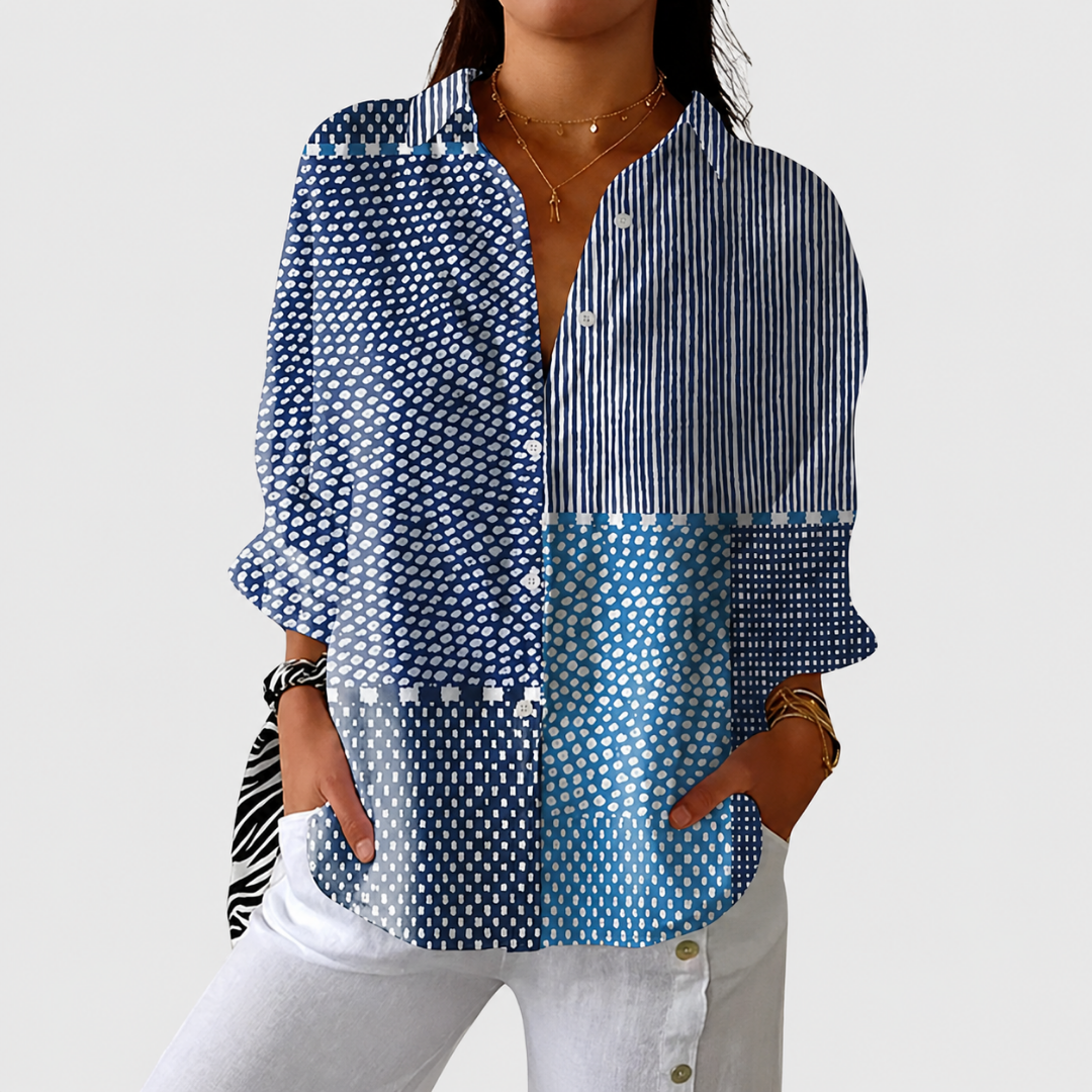 Model wearing the buttoned blouse in blue patchwork spots and stripes, hands in pockets of white trousers 1