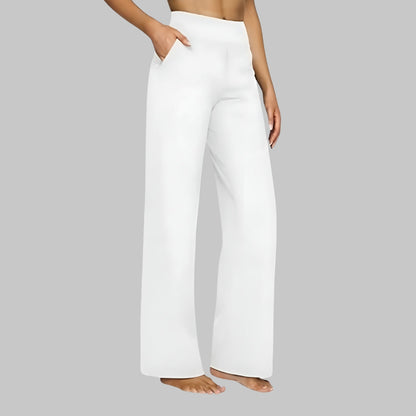Side view of the high-waist wide-leg trousers in white, worn by a barefoot model with a hand in the side pocket. 8