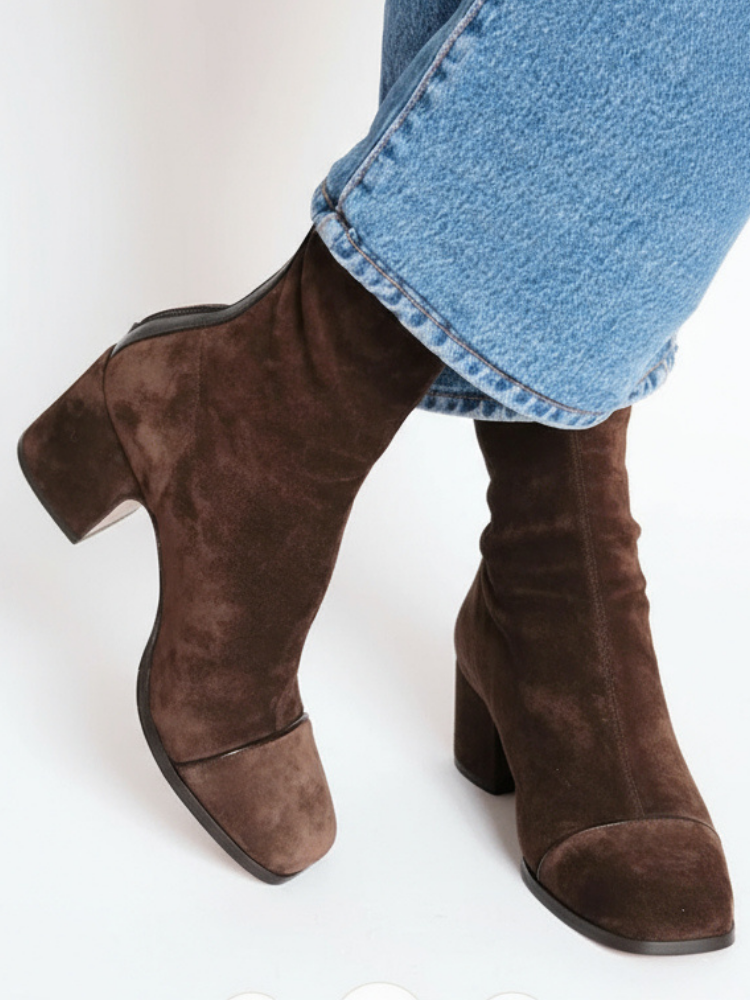 Dark brown suede block-heel ankle boots with contrast toe caps, worn with blue jeans, seen from a side-on angle. 1