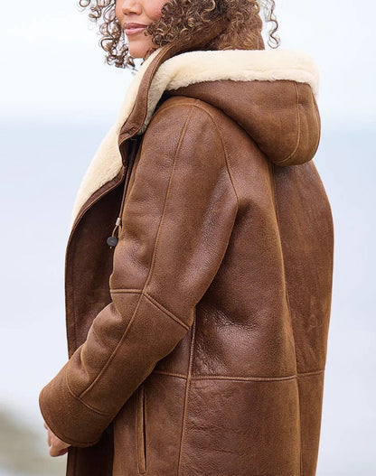 Side view of the coat on a model, showing the hood with cream fleece trim, the sleeve and the grained brown leather. 2