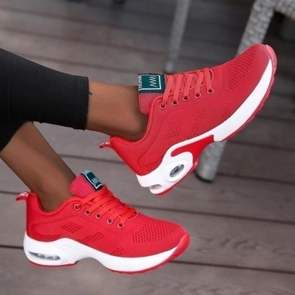 Red mesh trainers with white soles worn by a model in black leggings, feet raised to show the cushioned sole. 10