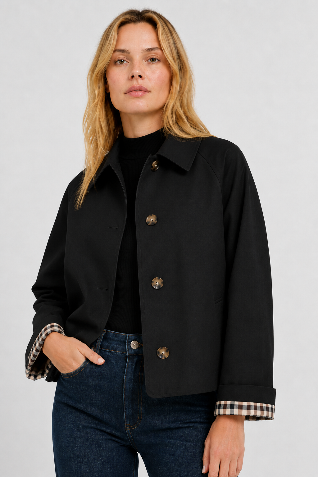 Model wears the black jacket open over a black top and jeans, one hand in pocket, gingham cuff lining visible. 19