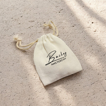 Cream drawstring pouch with a cotton cord, lying on a sandy textured surface in dappled light 5