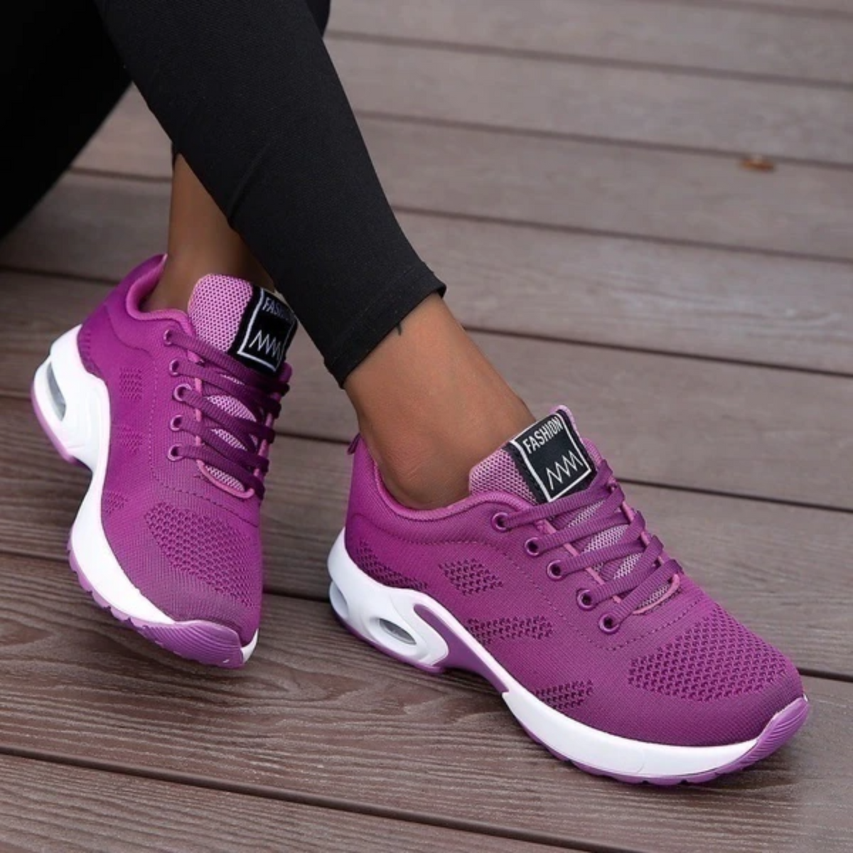 Purple mesh trainers with white air-cushioned soles worn by a model in black leggings, seated on wooden decking. 9
