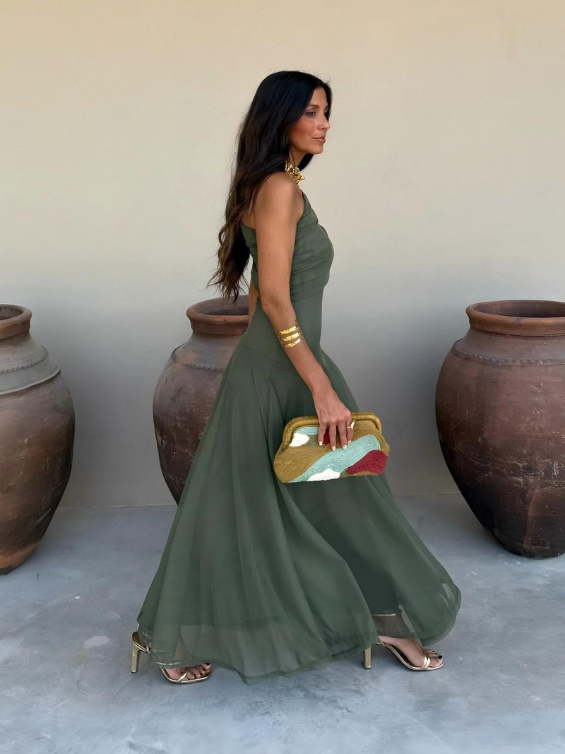 Side profile of olive green one-shoulder maxi dress with flowing skirt, model walking past large clay pots 9