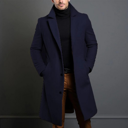 Model wearing the navy version of the single-breasted longline coat over a black roll-neck and tan trousers. 4