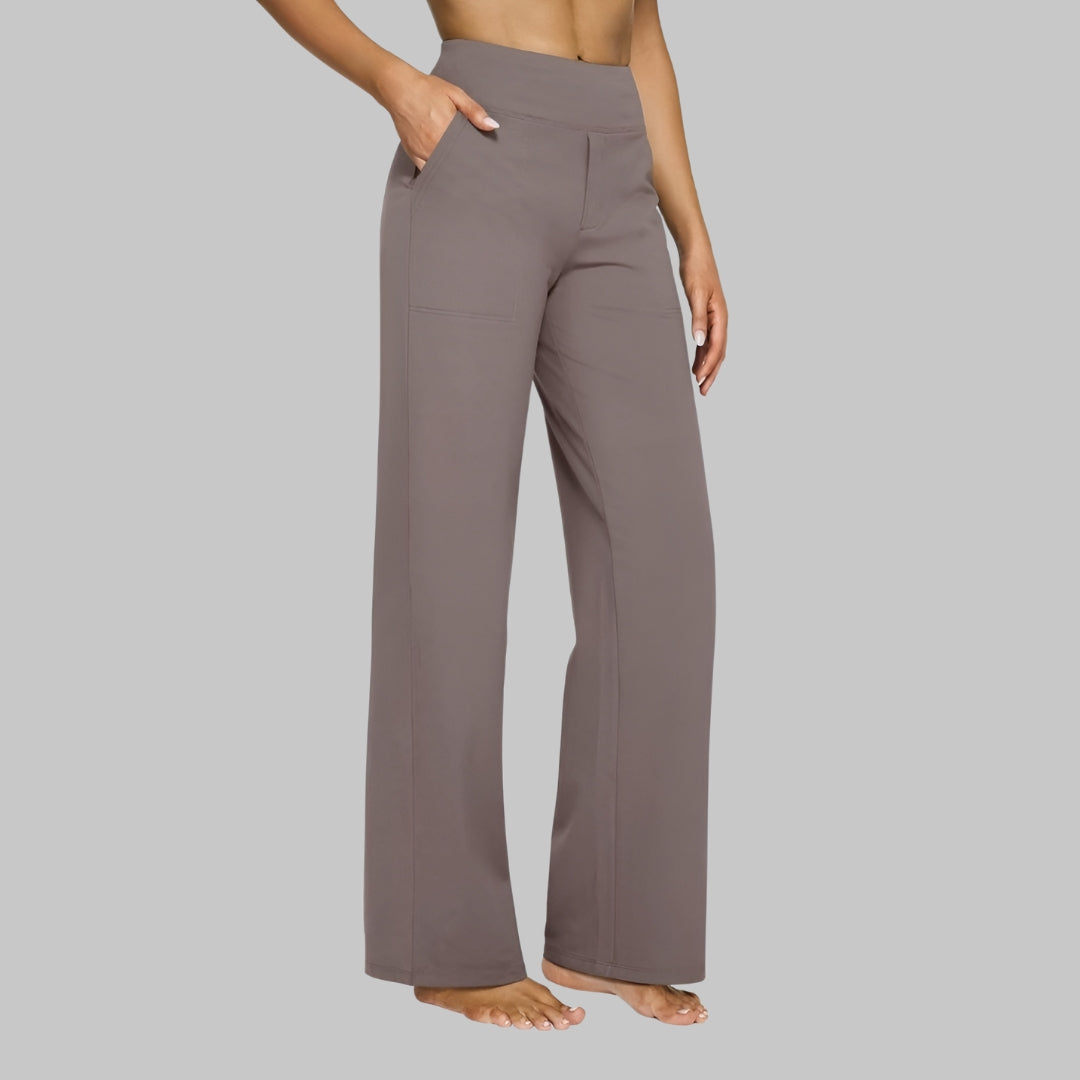 Model with one hand in a side pocket wears the high-waisted straight-leg trousers in taupe, seen from the front at an angle, barefoot. 1