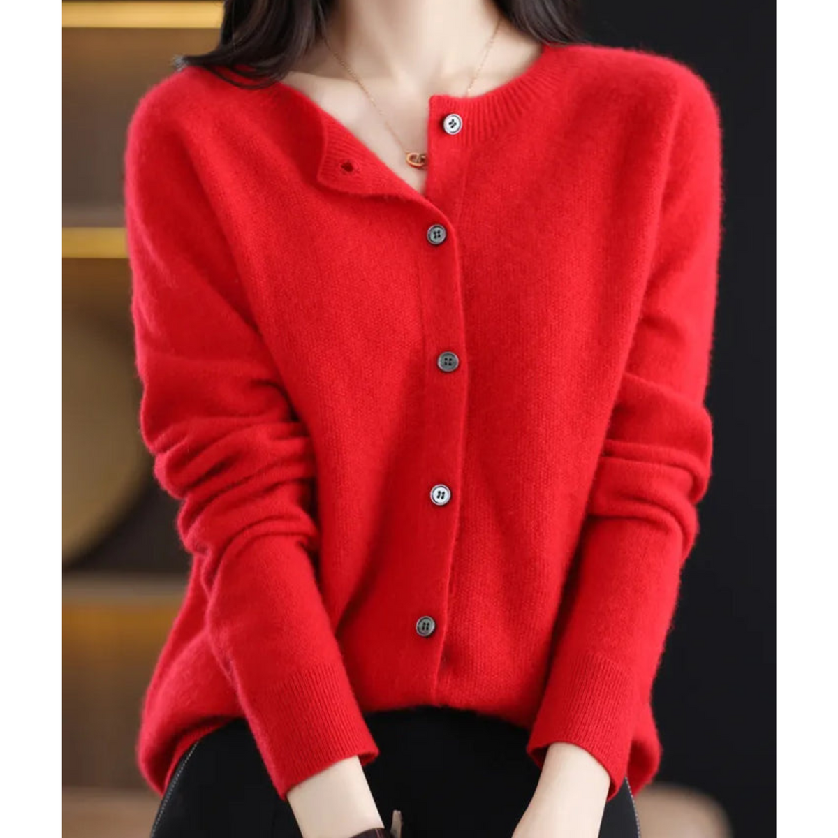 Bright red cardigan worn by a model sitting with hands in her lap, round neck partly unbuttoned and grey buttons down the front. 14