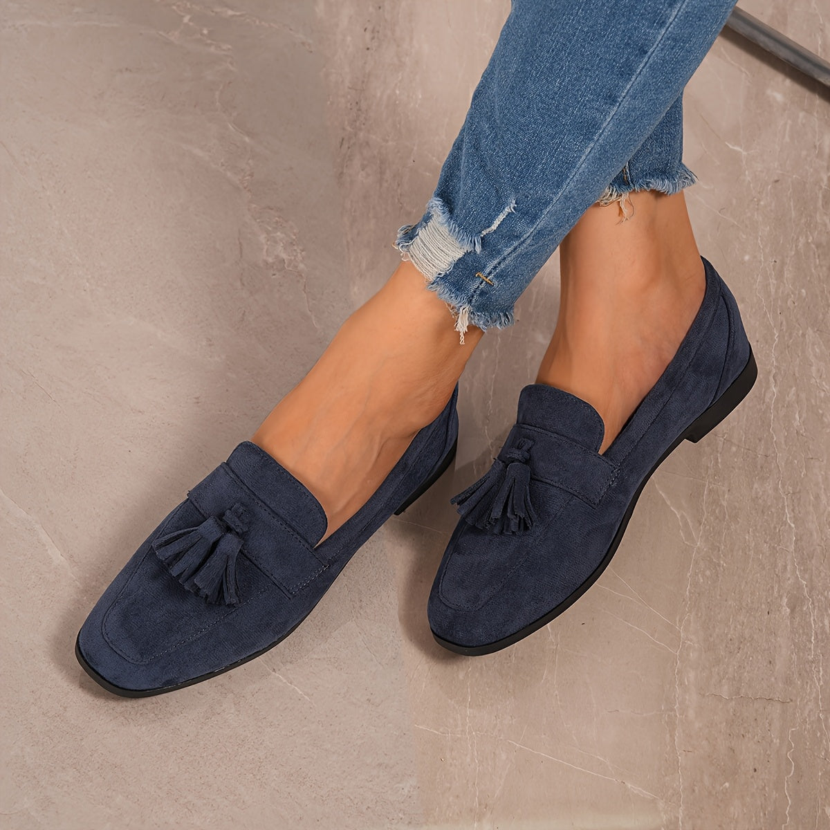 Navy tasselled loafers worn with frayed jeans, shot from above on a marble floor 7