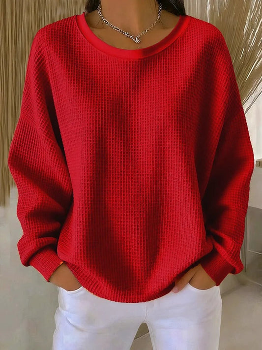 Model wearing the same waffle-knit jumper in red, with a round neckline and ribbed cuffs, over white trousers. 2
