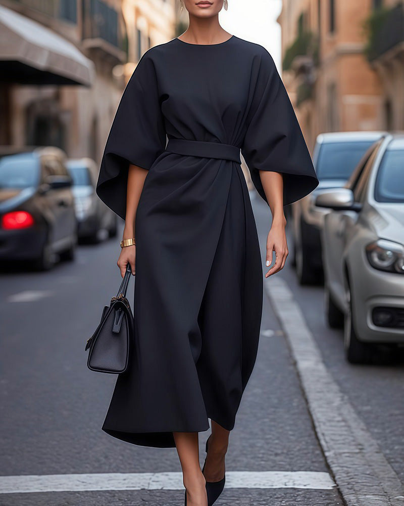 Full-length view of the black wrap-style midi dress worn on a city street with a black handbag 1