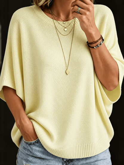 Close-up of the pale yellow knit batwing top with ribbed round neck, worn with layered gold necklaces and jeans. 4