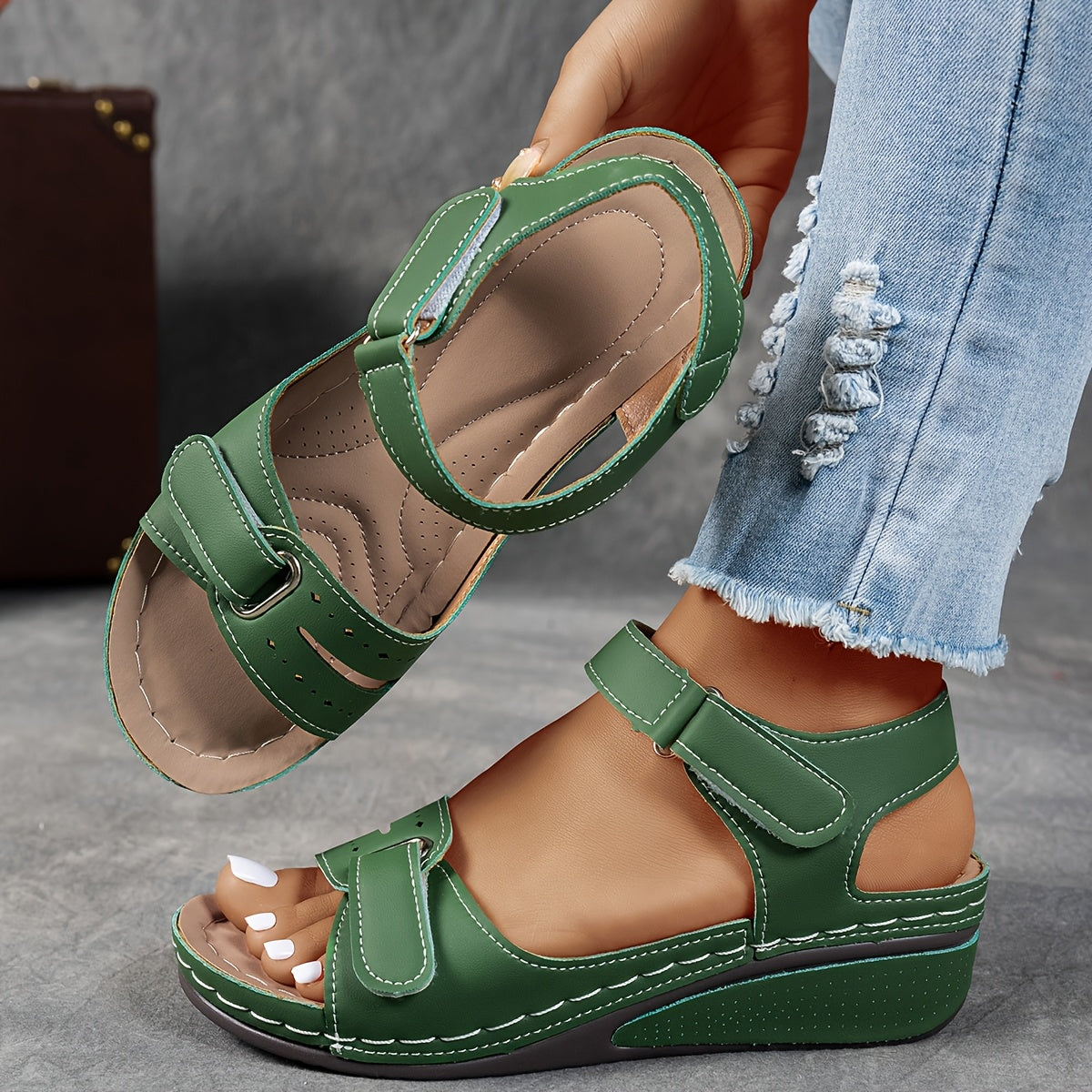 Green wedge sandals with adjustable straps, one on the foot and one lifted to reveal the cushioned, perforated footbed. 3
