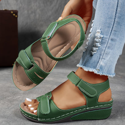 Green wedge sandals with adjustable straps, one on the foot and one lifted to reveal the cushioned, perforated footbed. 3