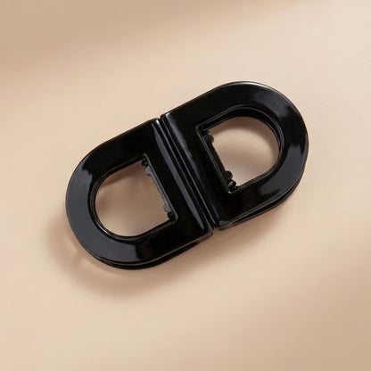 Glossy black oval flat hair clip with two open halves and a visible inner clasp, shown from above. 6