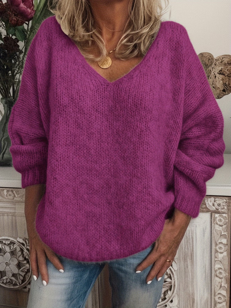 Woman wearing the soft knit V-neck jumper in magenta purple, front view, with a gold pendant necklace and jeans. 6