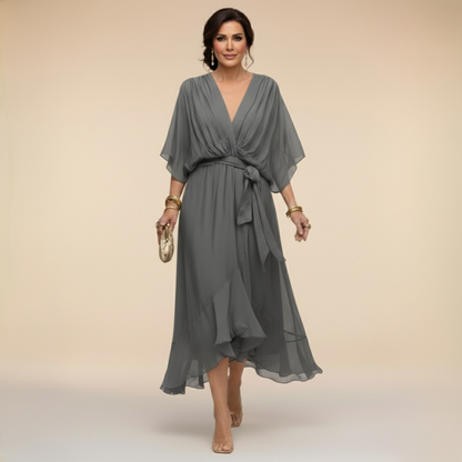 Model wearing the grey chiffon midi dress with draped V-neck, wide sleeves, waist sash and tiered ruffle hem, carrying a gold clutch. 10