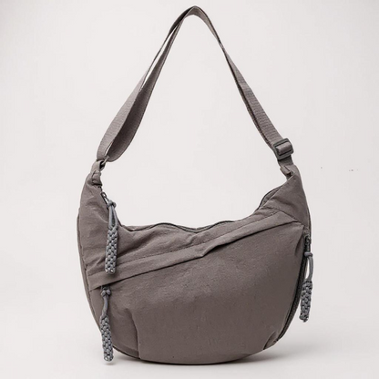 Grey crescent shoulder bag from the front, with braided zip pulls and an adjustable strap, on a pale background. 10