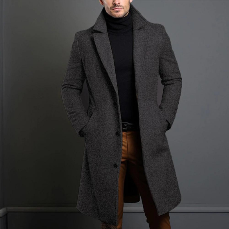 Model wearing the dark grey, textured version of the long tailored coat with a black roll-neck, hands in the pockets. 3