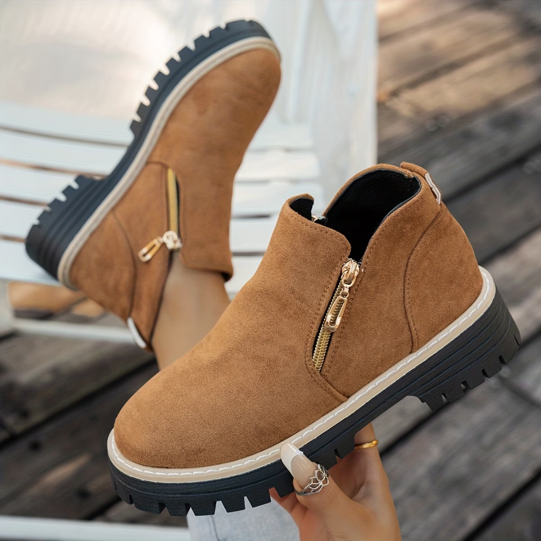 Tan brown suede-look ankle boots with gold side zips and chunky black treaded soles, worn by a model outdoors. 4