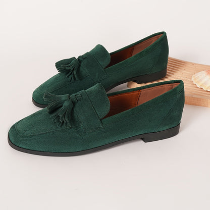 Pair of green tasselled loafers with tan lining on a plain surface, shell beside them 8