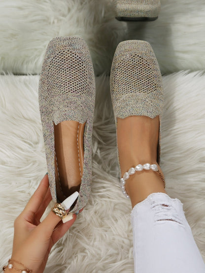 Top-down view of speckled beige knit slip-on shoes with perforated mesh toes, one worn with a pearl anklet, one held to show the cushioned footbed. 21