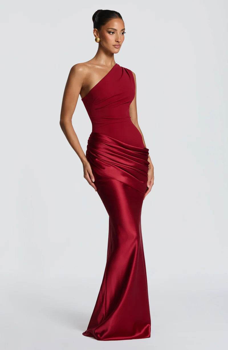 Three-quarter side view of the deep red one-shoulder dress, showing the gathered satin hip drape and long fluid skirt. 22