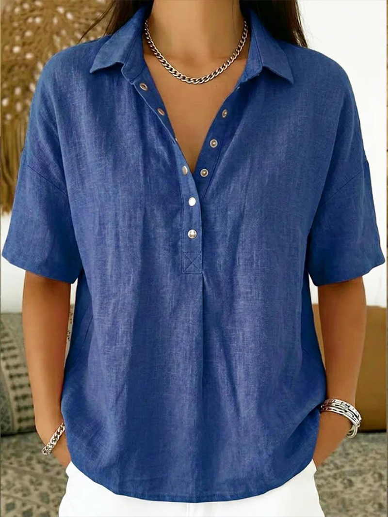 Short-sleeved blouse in royal blue, worn by a model with a silver chain necklace and white trousers 1