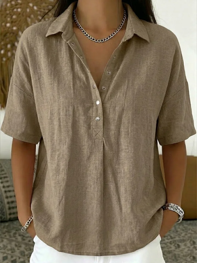 Short-sleeved blouse in taupe-beige, worn by a model with a chain necklace and white trousers 2