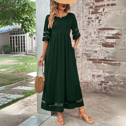 Dark green version of the maxi dress worn with a straw hat and woven round bag, hand resting in a pocket. 6