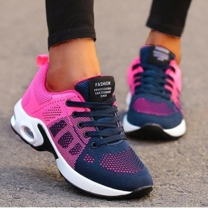 Pink and navy mesh trainers worn by a model in black leggings, walking on tarmac to show the air-cushioned sole. 12