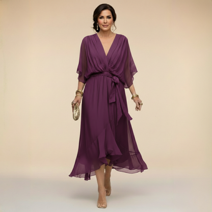 Model walking in the plum purple chiffon midi dress with wrap-effect V-neck, sheer sleeves, bow-tied waist and ruffled flowing hem. 9