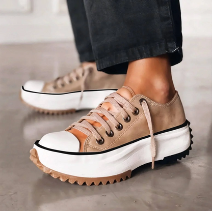 Side view of beige lace-up platform trainers worn with black trousers, showing the chunky white sole and zigzag gum tread. 1