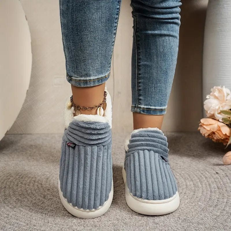 Front view of blue-grey ribbed slippers worn by a model in jeans, standing on a grey rug. 11