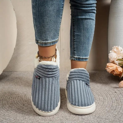 Front view of blue-grey ribbed slippers worn by a model in jeans, standing on a grey rug. 11