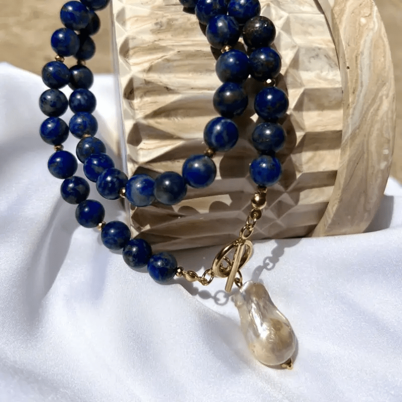 Strands of blue beads curved around a carved wooden block, with the pearl pendant resting on white cloth 9