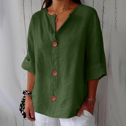 Model wearing the loose blouse in olive green, with three brown buttons, notched V-neck and cuffed sleeves, hand tucked in white trousers. 12