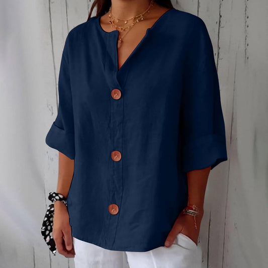 Model wearing the loose button-front blouse in navy blue, rolled half sleeves and notched V-neckline, styled with white trousers and a spotted scrunchie. 2
