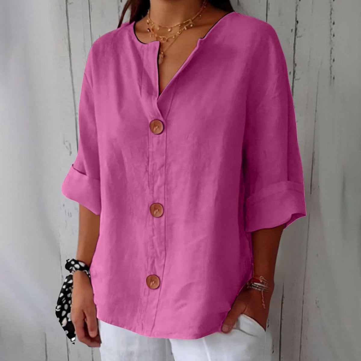 Model wearing the loose button-front blouse in bright pink, with notched V-neck, rolled half sleeves and a spotted scrunchie on her wrist. 8