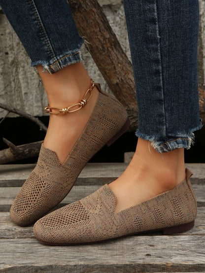 Side view of brown knit mesh slip-ons with a low flat heel, worn with frayed denim jeans on wooden boards. 5