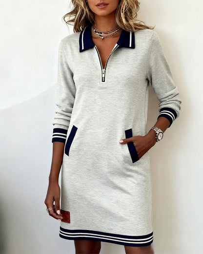 Light grey dress on a model, one hand tucked into a navy-trimmed pocket, half-zip open at the neckline. 3