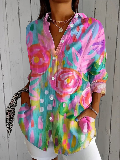 Model wearing the buttoned shirt with large painted pink roses on a turquoise and yellow ground, hands in pockets. 1