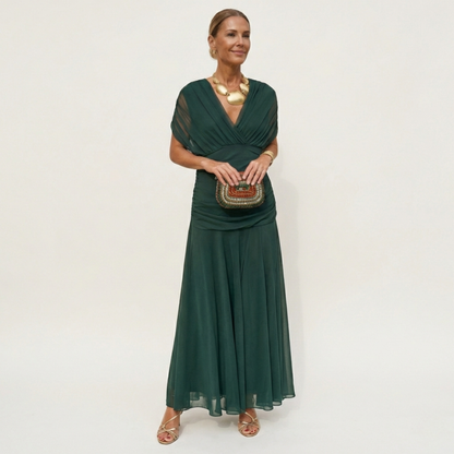 Model in a full-length dark green chiffon dress with a ruched V-neck bodice and sheer cap sleeves, holding a beaded clutch. 1