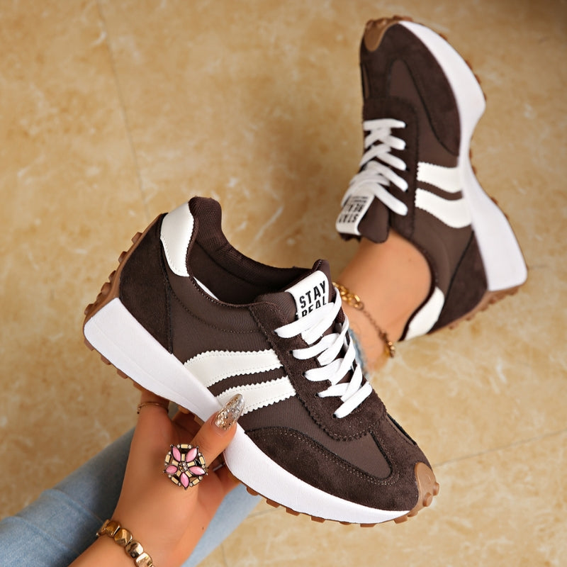 Dark brown trainers with white stripes and chunky white platform soles, held in a hand and worn 3