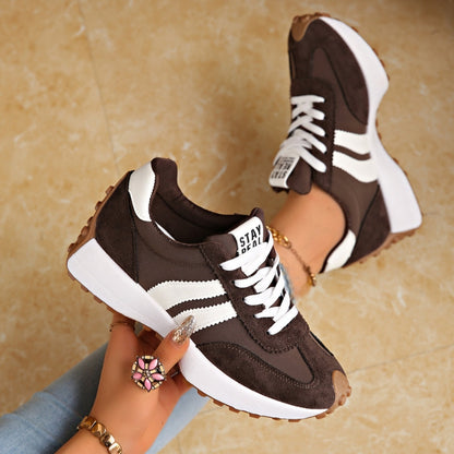 Dark brown trainers with white stripes and chunky white platform soles, held in a hand and worn 3