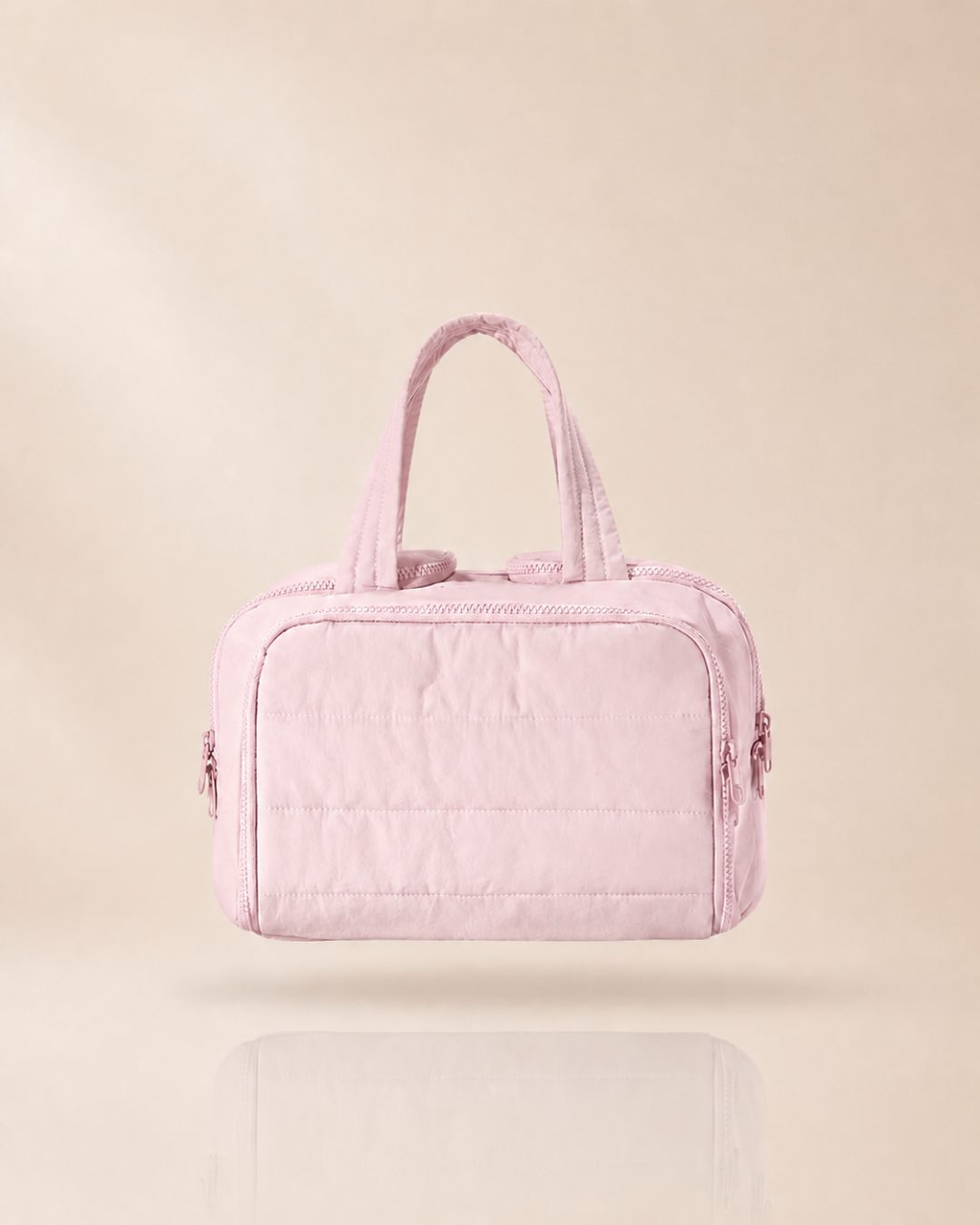 Pink quilted organiser bag with two handles, front view on a soft beige background with a faint reflection. 11