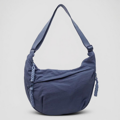 Slate blue crescent shoulder bag from the front, with braided zip pulls and a matching adjustable strap, on a light background. 9